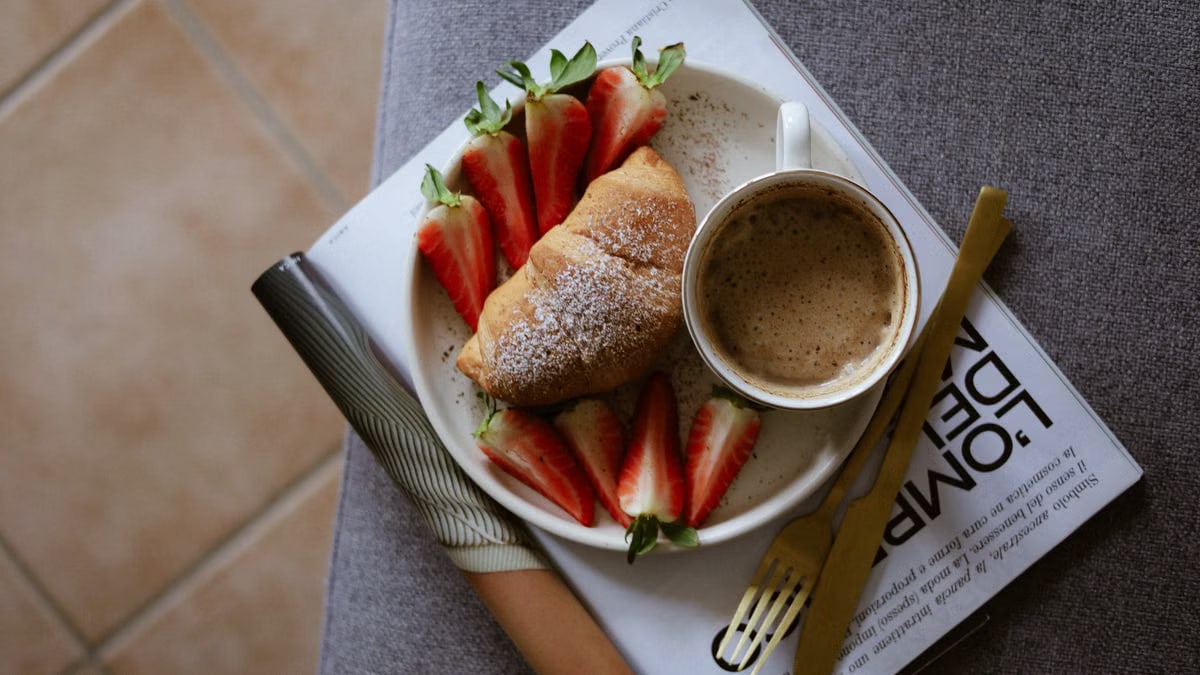 A cozy breakfast setup with croissant, strawberries, and coffee on a magazine.