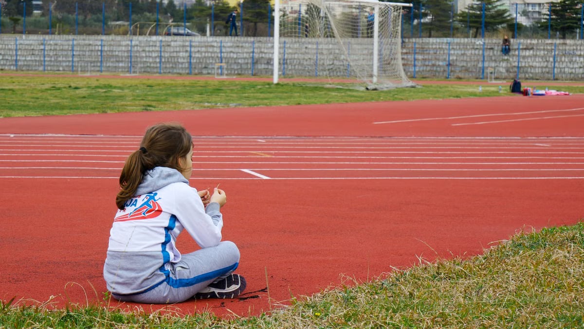 Young girl resting by a running track on a sunny day. Capturing a moment of reflection.